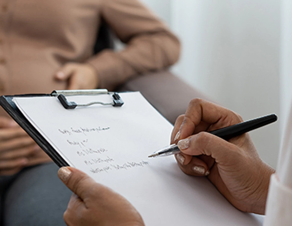 Doctor with clip board, taking notes on a pregnant patient who is seated in the backgroud.